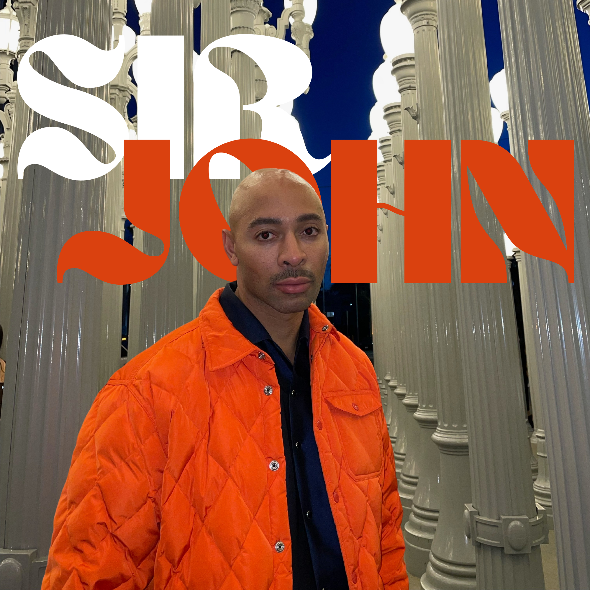 Sir John in an orange quilted jacket in front of columns. The text in the background reads SIR JOHN.