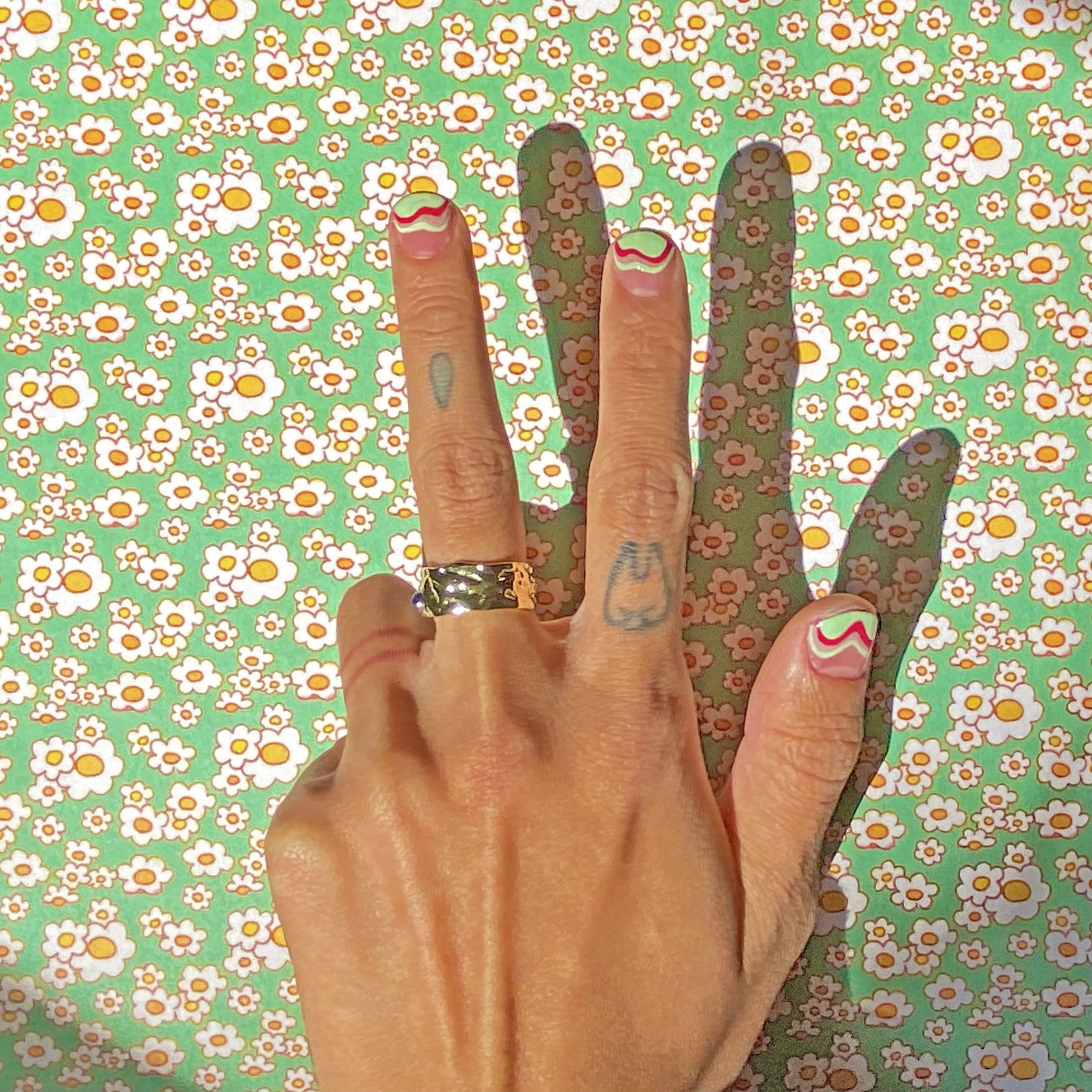 Male hands with tattoos, 70's-inspired wave nail art and gold rings using Harry Styles' Pleasing Shroom Bloom polish