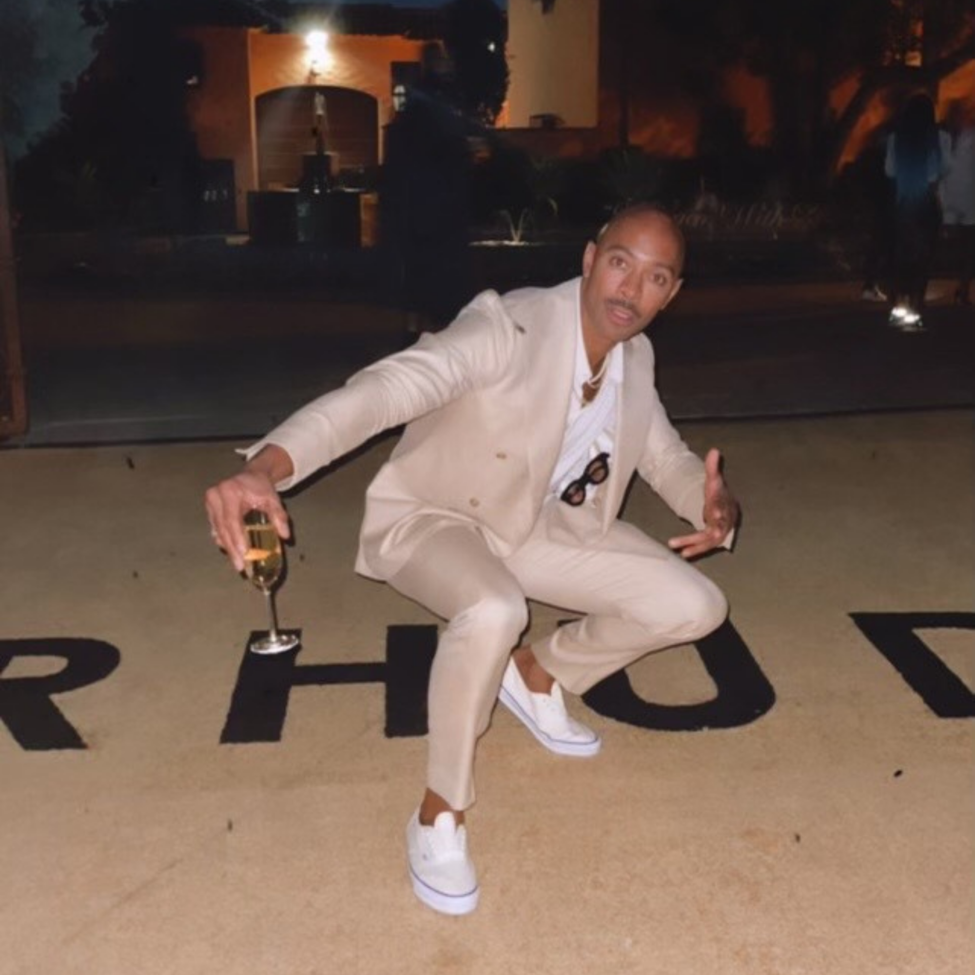 Sir John in a tan suit with a champagne flute, posing