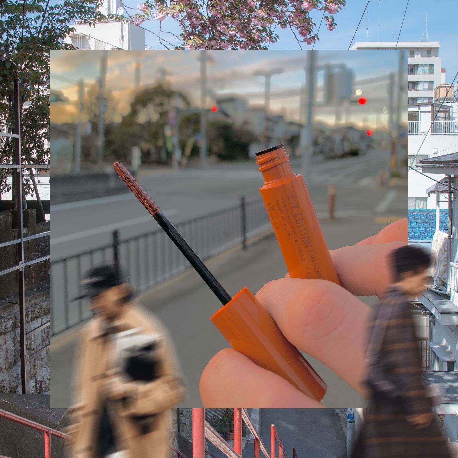 Tube of orange mascara against a photo of a Japanese neighborhood