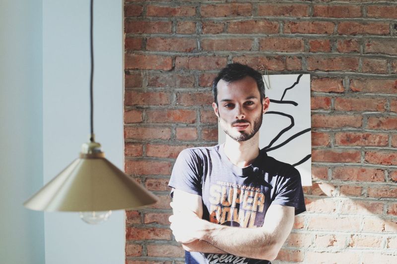 Brick wall background. White man standing with arms crossed in casual t-shirt. 