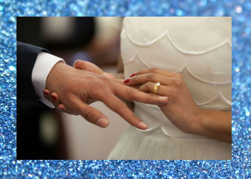 Blue glitter background. Wife putting ring on husband at wedding. 