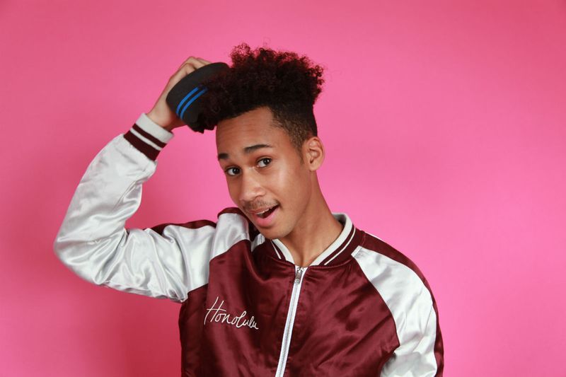 Pink background. Black man brushing his hair with sponge. 